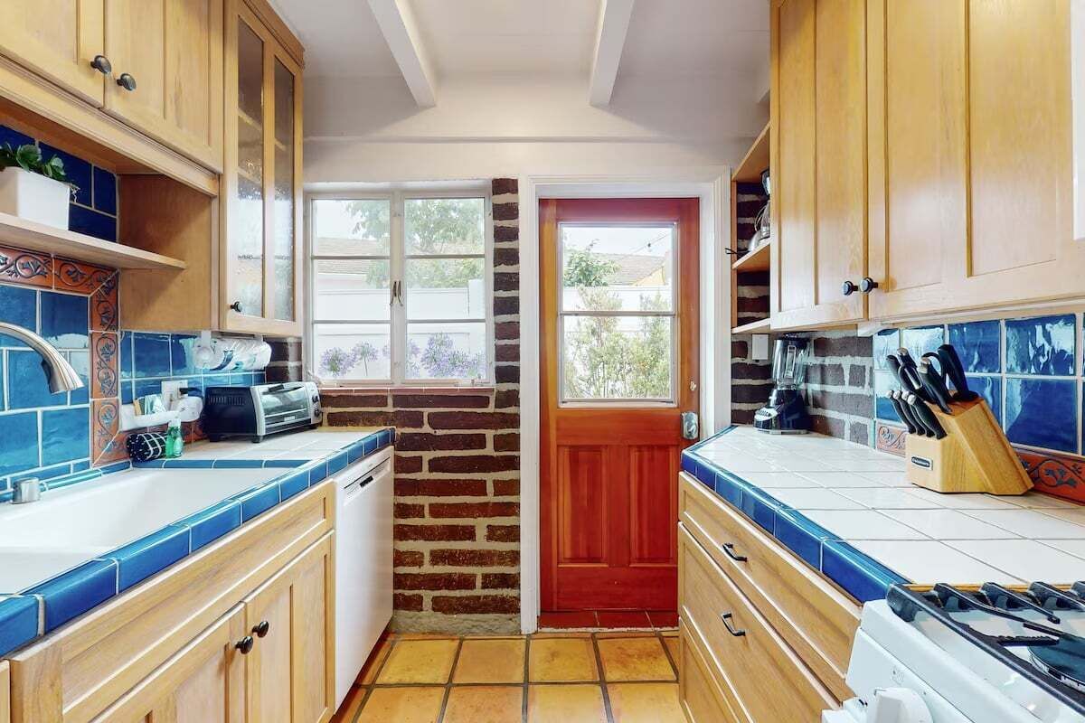 A kitchen with wooden cabinets, a brick wall, a red door, and a window.