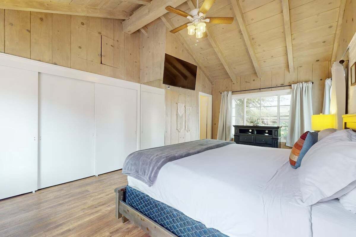 A wooden-paneled bedroom with a bed, a ceiling fan, and a window with curtains.