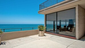 Ein modernes Gebäude mit einem Balkon mit Meerblick, großen Glasfenstern und Sitzgelegenheiten im Freien.
