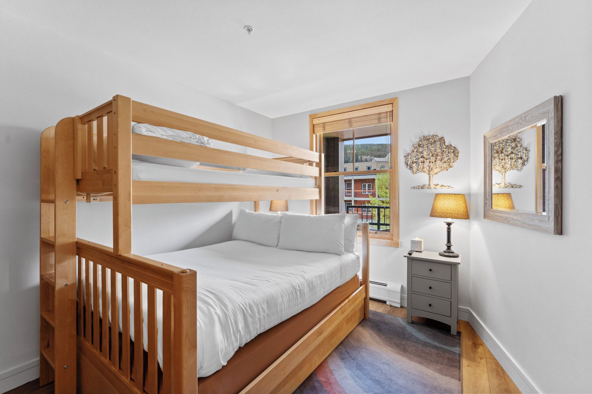 Een houten stapelbed in een kamer met een raam, een nachtkastje en een lamp.