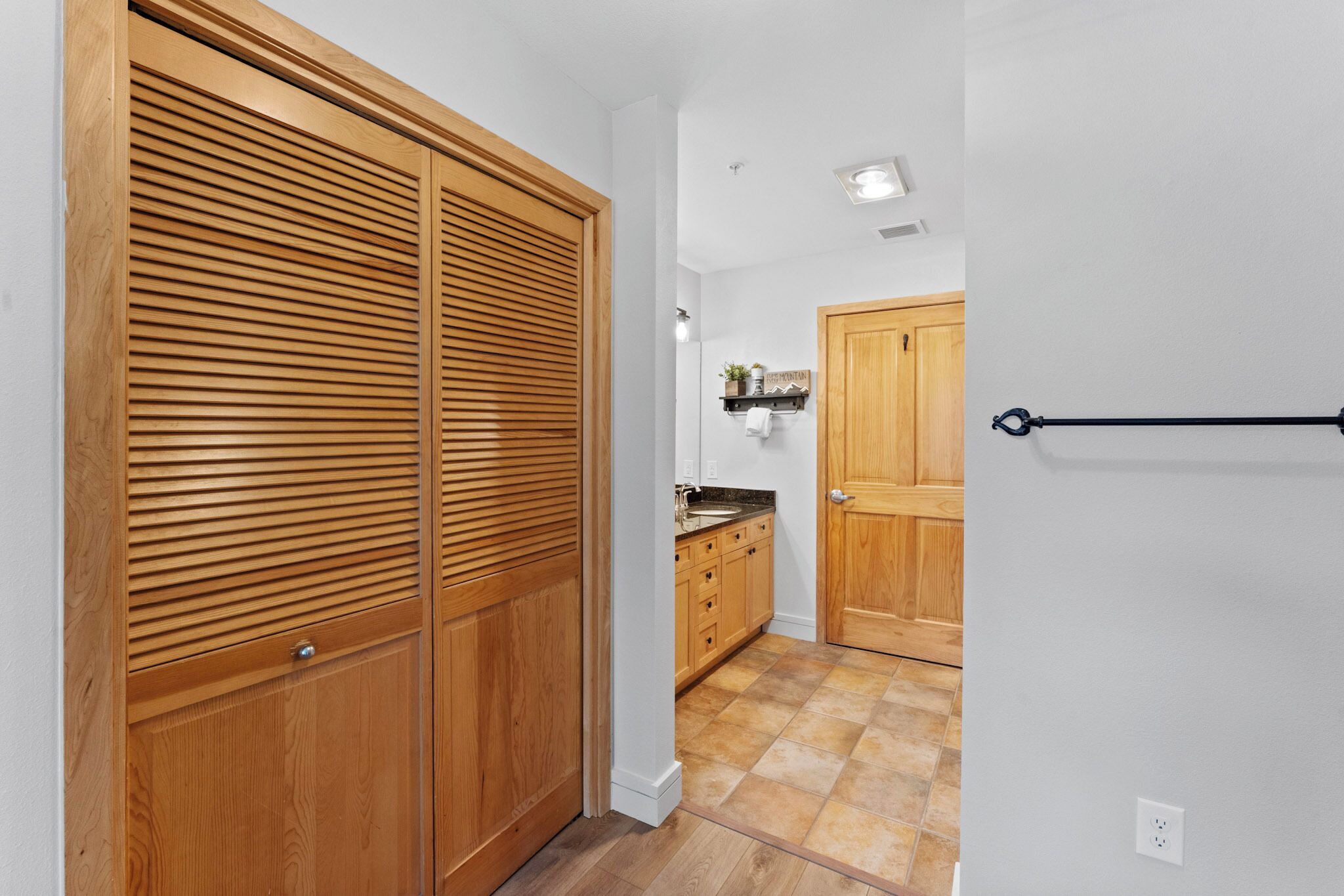 A hallway with wooden sliding doors, a kitchen area with wooden cabinets, and a tiled floor.