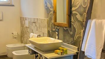 A bathroom with a sink, toilet, and bidet, a mirror, and a decorative wall.