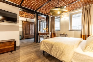 A bedroom with a brick ceiling, a bed with a white bedspread, a wooden dresser, a desk with a chair, and a window with curtains.