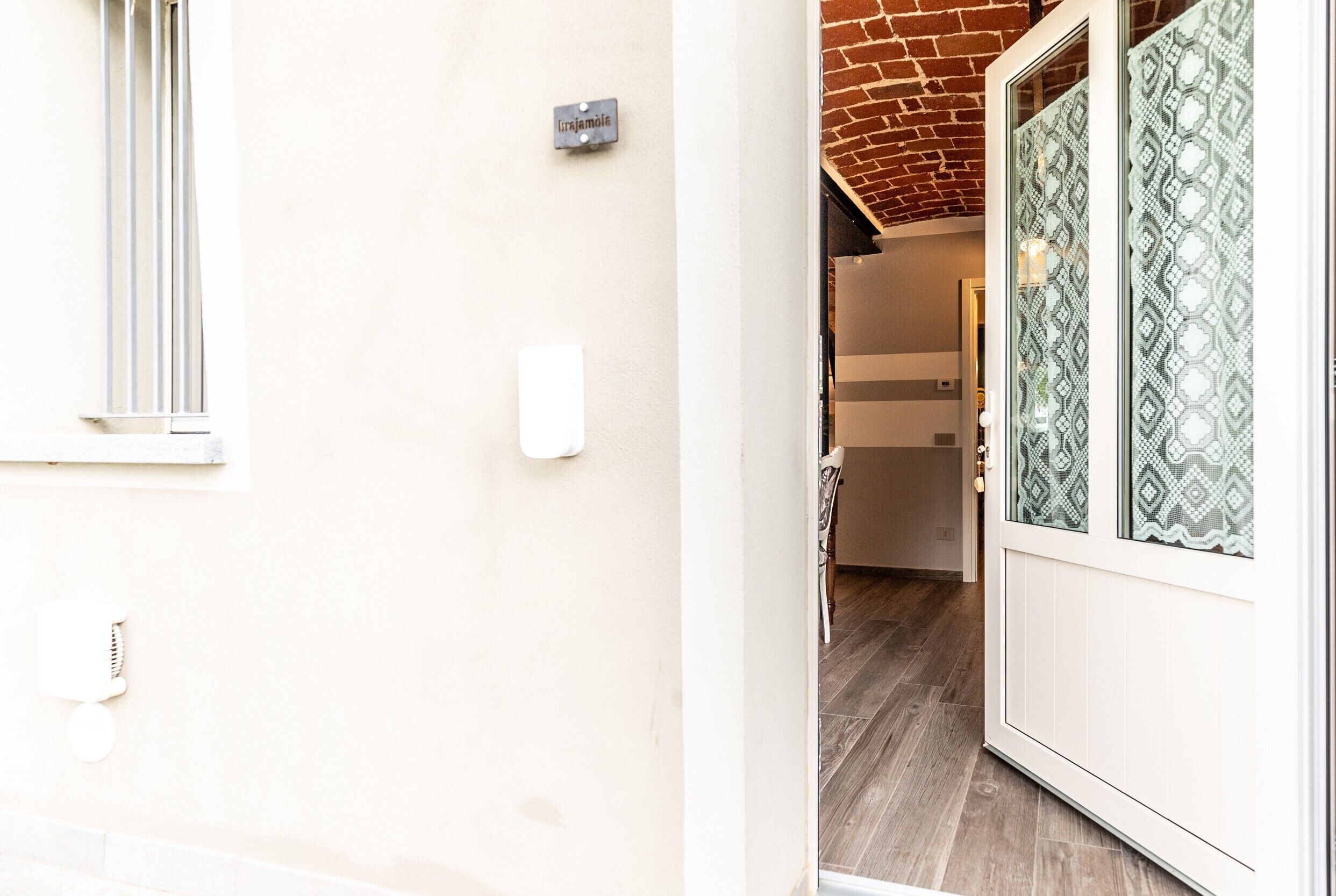 A hallway with a white door, a window with blinds, a wall-mounted light switch, and a door with patterned glass.