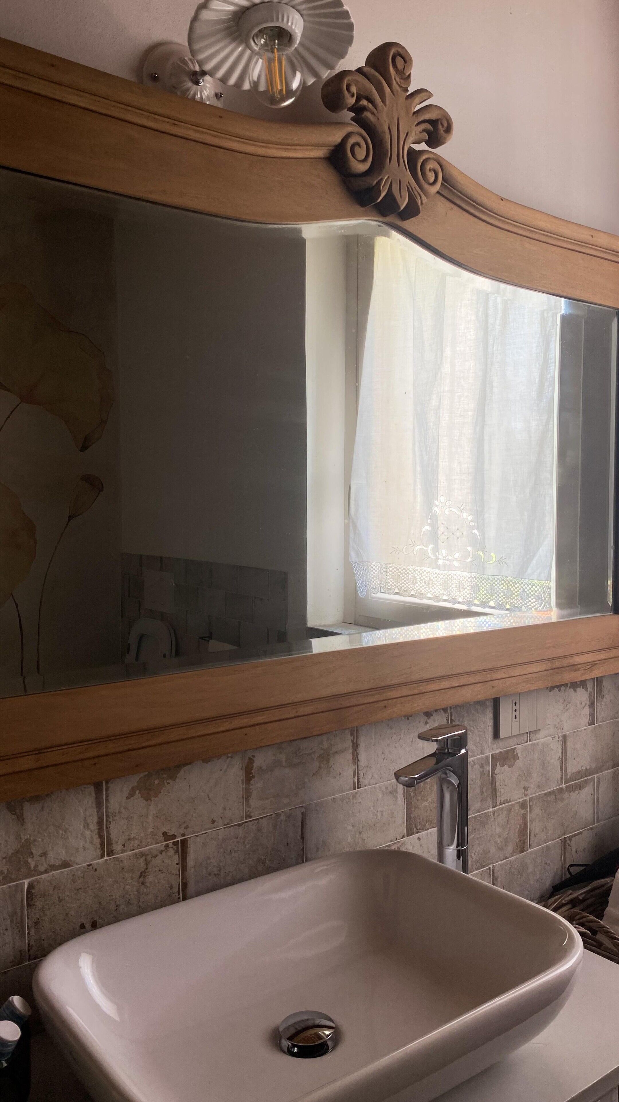 A bathroom with a white sink, a mirror with a wooden frame, and a window with a lace curtain.