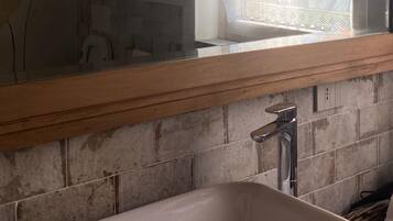 A bathroom with a white sink, a mirror with a wooden frame, and a window with a lace curtain.