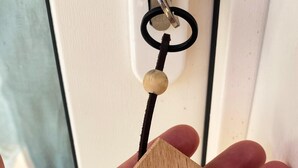 Een hand houdt een houten sleutelhanger met een huisvormige bedel en de tekst 'pistapeijvri' erop.