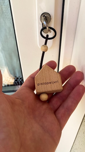 A hand holding a wooden keychain with a house-shaped pendant and the text 'pistapeijvri' on it. - Room 'Pistapeijvri' with Private Garden, Wi-Fi, and Air Conditioning (Quargnento)