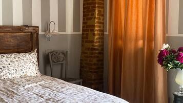 A bedroom with a bed, a nightstand, a lamp, a brick wall, and a window with curtains.