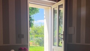 Een slaapkamer met een bed, een dressoir, een stoel, een vaas met bloemen en een deur die uitkomt op een tuin.