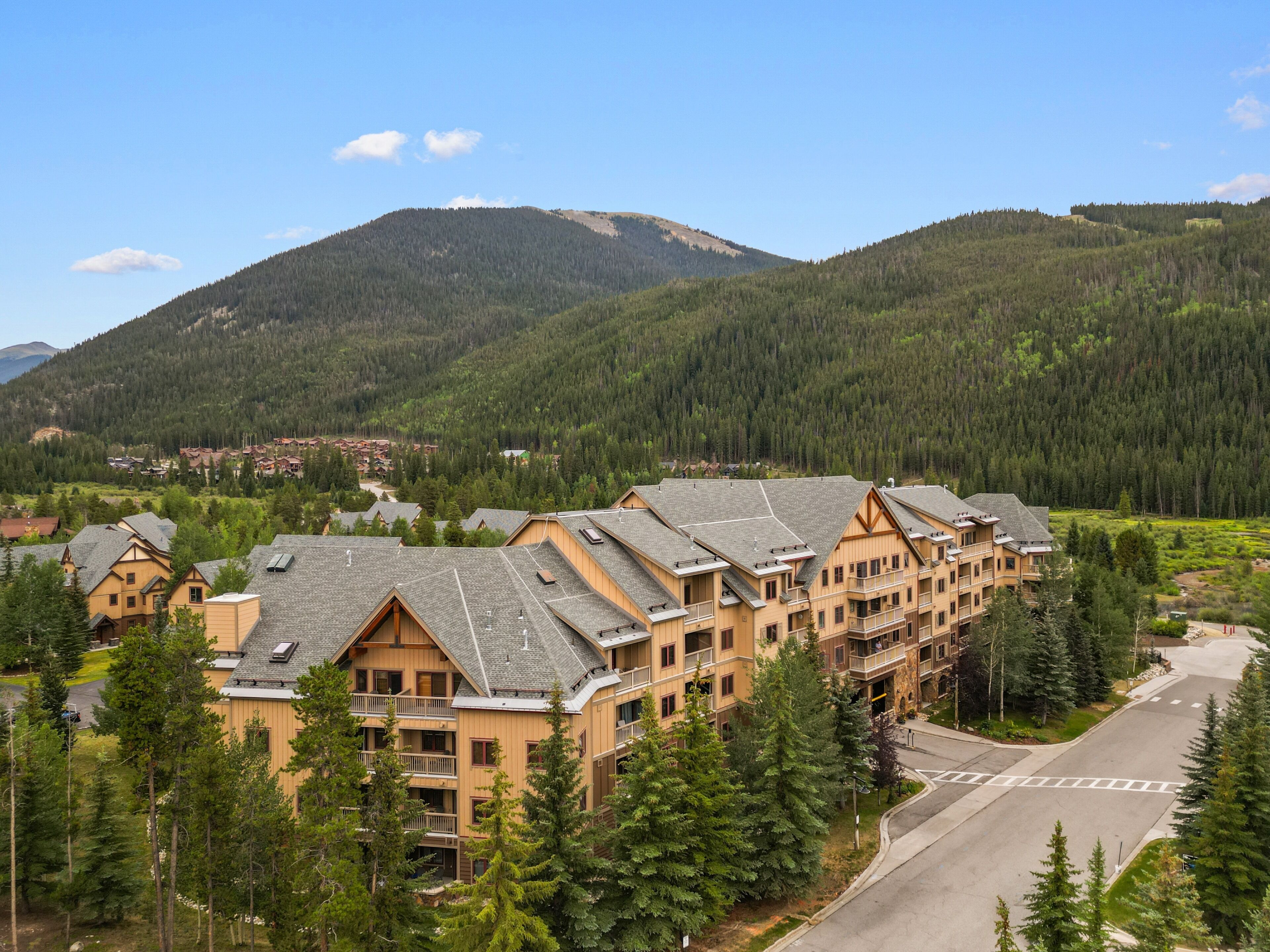 Un hôtel à plusieurs étages, de style architectural traditionnel, entouré d’un paysage boisé et avec des montagnes en toile de fond.