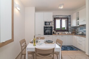 A modern kitchen with white cabinetry, a dining table set for four, and a view of the outdoors through a window.