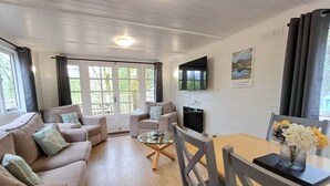 Ein modernes Wohnzimmer mit einer Sofagarnitur, einem Couchtisch und einem Esstisch mit Stühlen. An der Wand hängt ein Flachbildfernseher, darüber ein Gemälde.