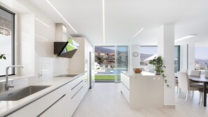 A modern kitchen with a large island, a dining area with a table and chairs, and a view of a mountainous landscape through large windows. - Private Villa with Heated Pool, Air Conditioning, and Football Field (Candelaria)