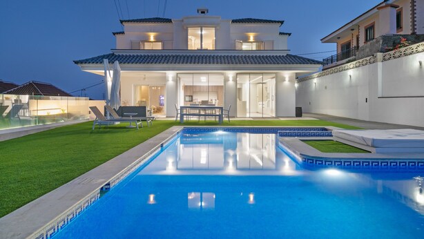 A modern house with a swimming pool, a patio with chairs, and a well-lit interior. - Private Villa with Heated Pool, Air Conditioning, and Football Field (Candelaria)