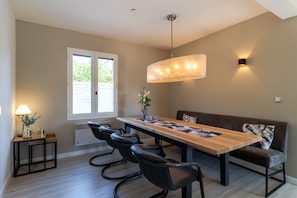 A dining area with a long wooden table, black chairs, a bench, a pendant light, and a wall-mounted light fixture. - Holiday Home 'Fleurie' with Shared Pool, Wi-Fi & Air Conditioning (Castelnaud-la-Chapelle)