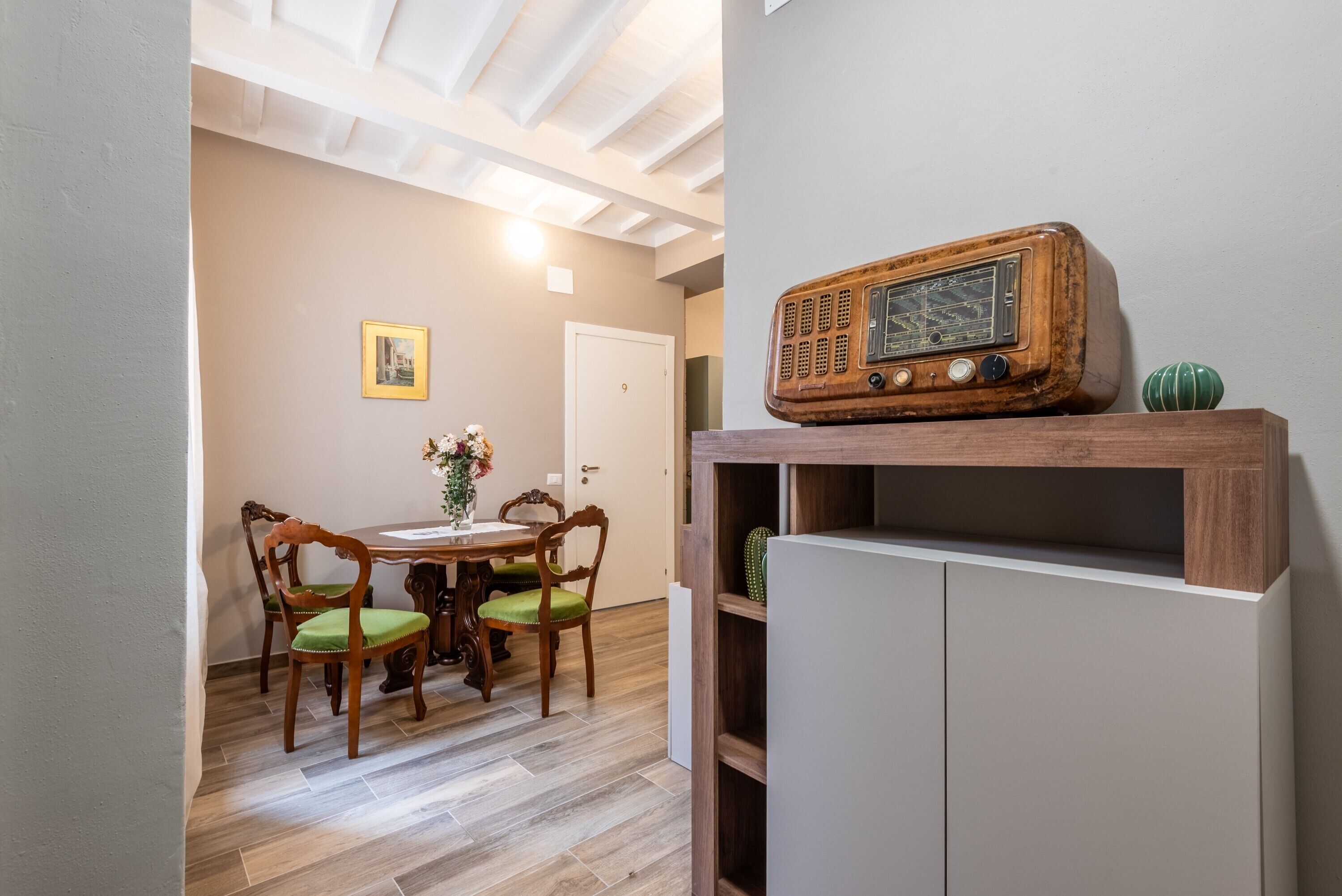 Un comedor con una mesa y sillas de madera, una radio antigua en un estante y una puerta al fondo.