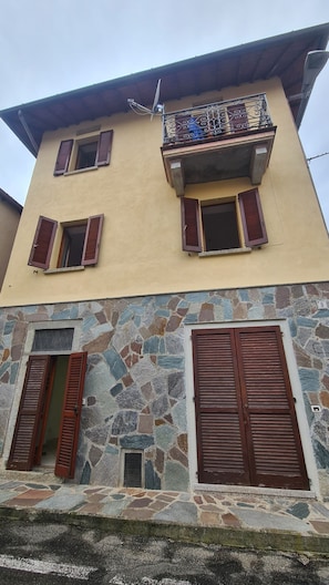 Un immeuble de deux étages doté d’un balcon, d’une façade en pierre et de volets en bois.