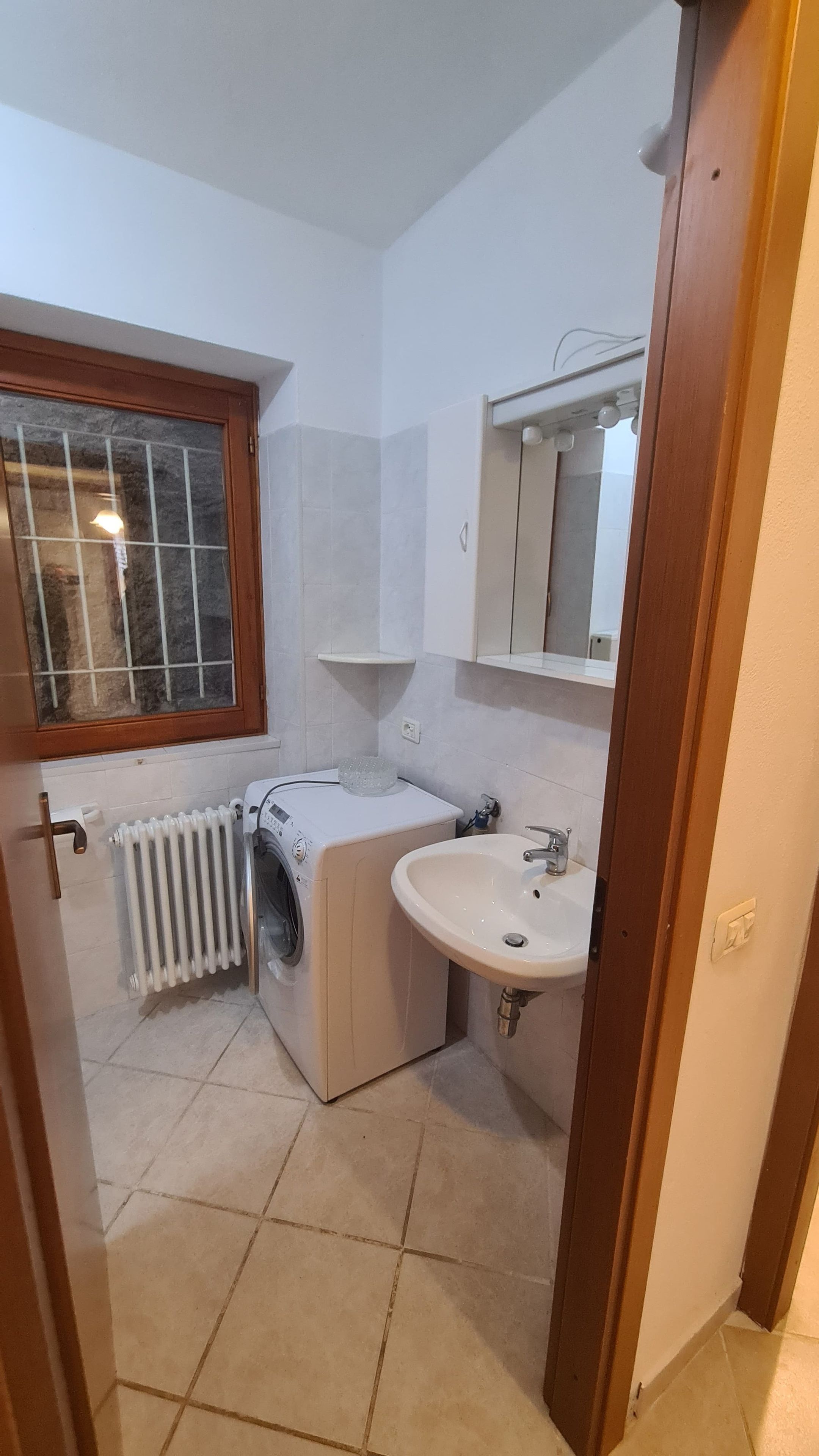 Ein kleines Badezimmer mit Heizkörper, Waschmaschine, Waschbecken und einem Fenster mit Gitterstäben.