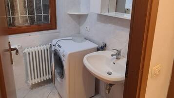 Ein kleines Badezimmer mit Heizkörper, Waschmaschine, Waschbecken und einem Fenster mit Gitterstäben.