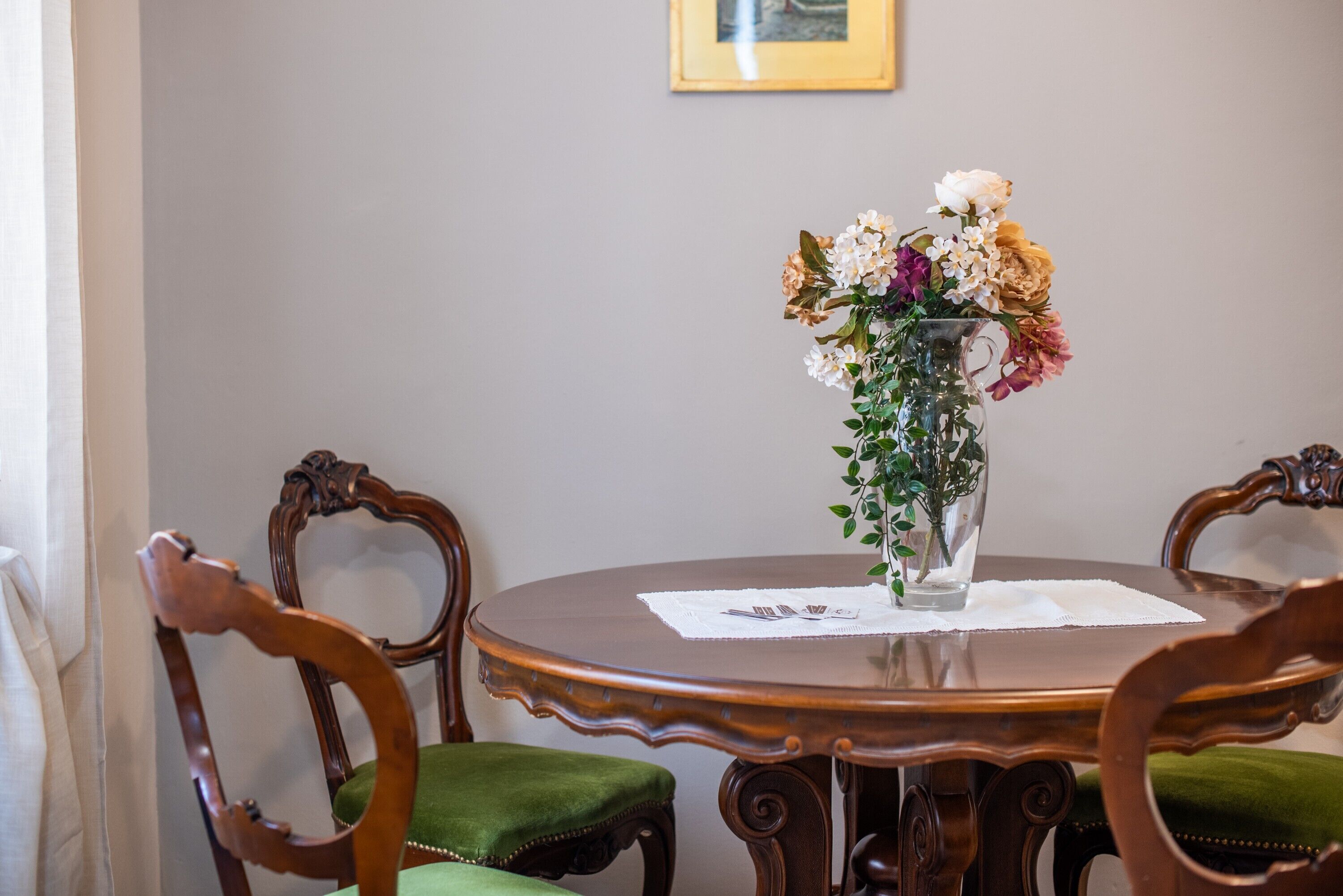 A dining table with a vase of flowers, surrounded by wooden chairs with green upholstery.