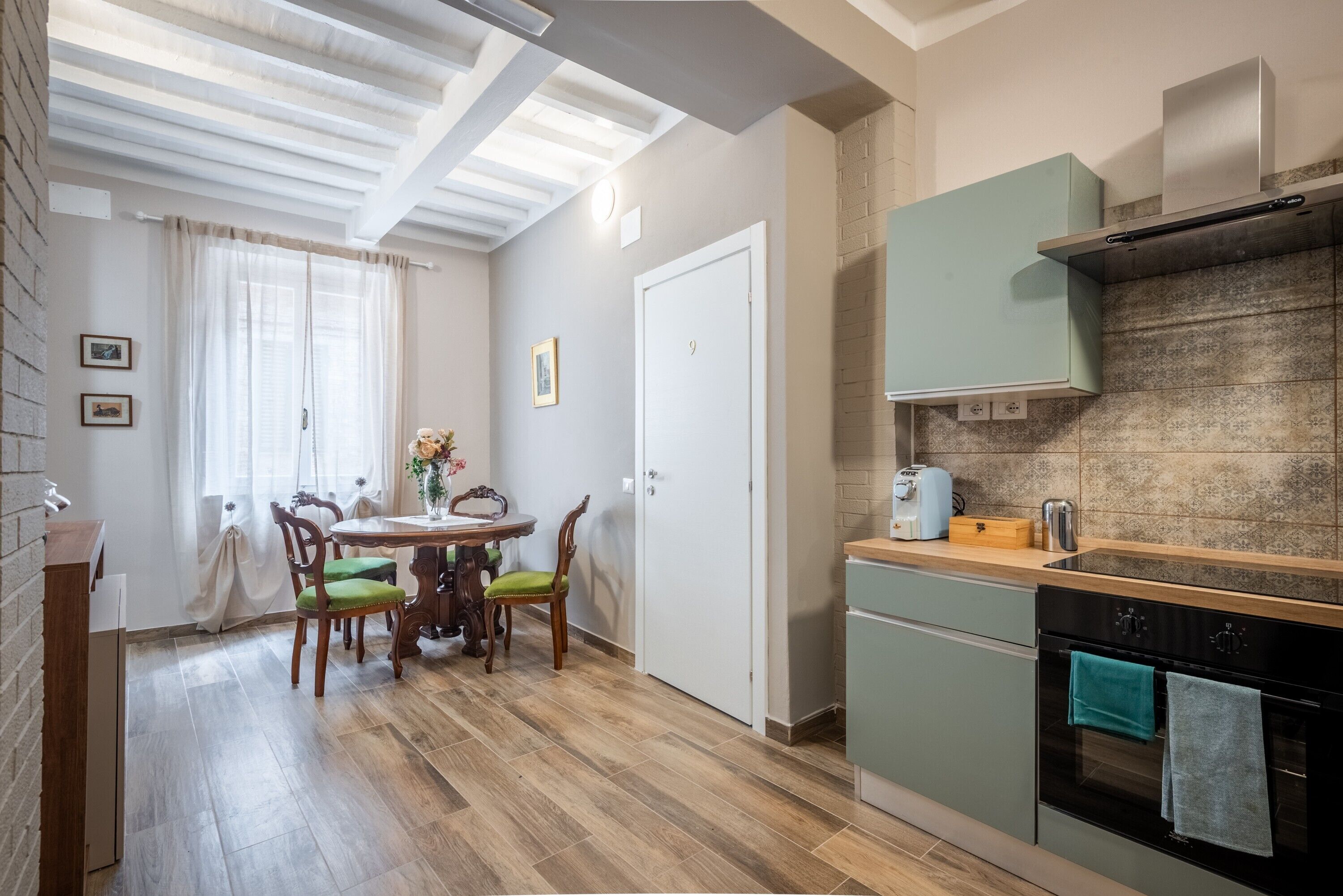 Een keuken met een inbouwoven, een eethoek met een tafel en stoelen, en een deur met een nummer.