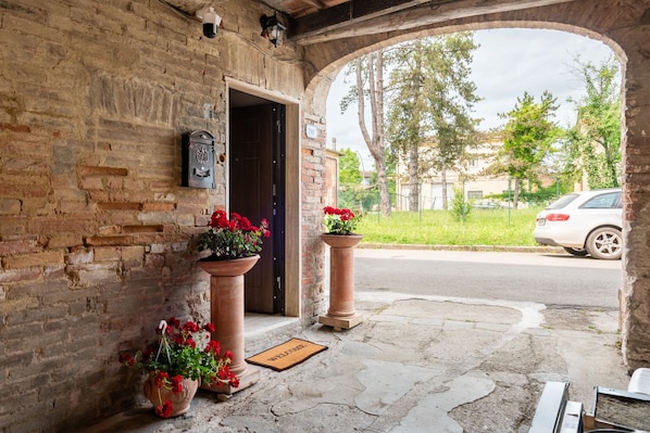 A brick building entrance with a welcome mat, potted red flowers, and a mailbox.