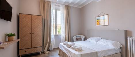 Une chambre à coucher avec un lit, une armoire, une chaise, un téléviseur et une fenêtre avec des rideaux.