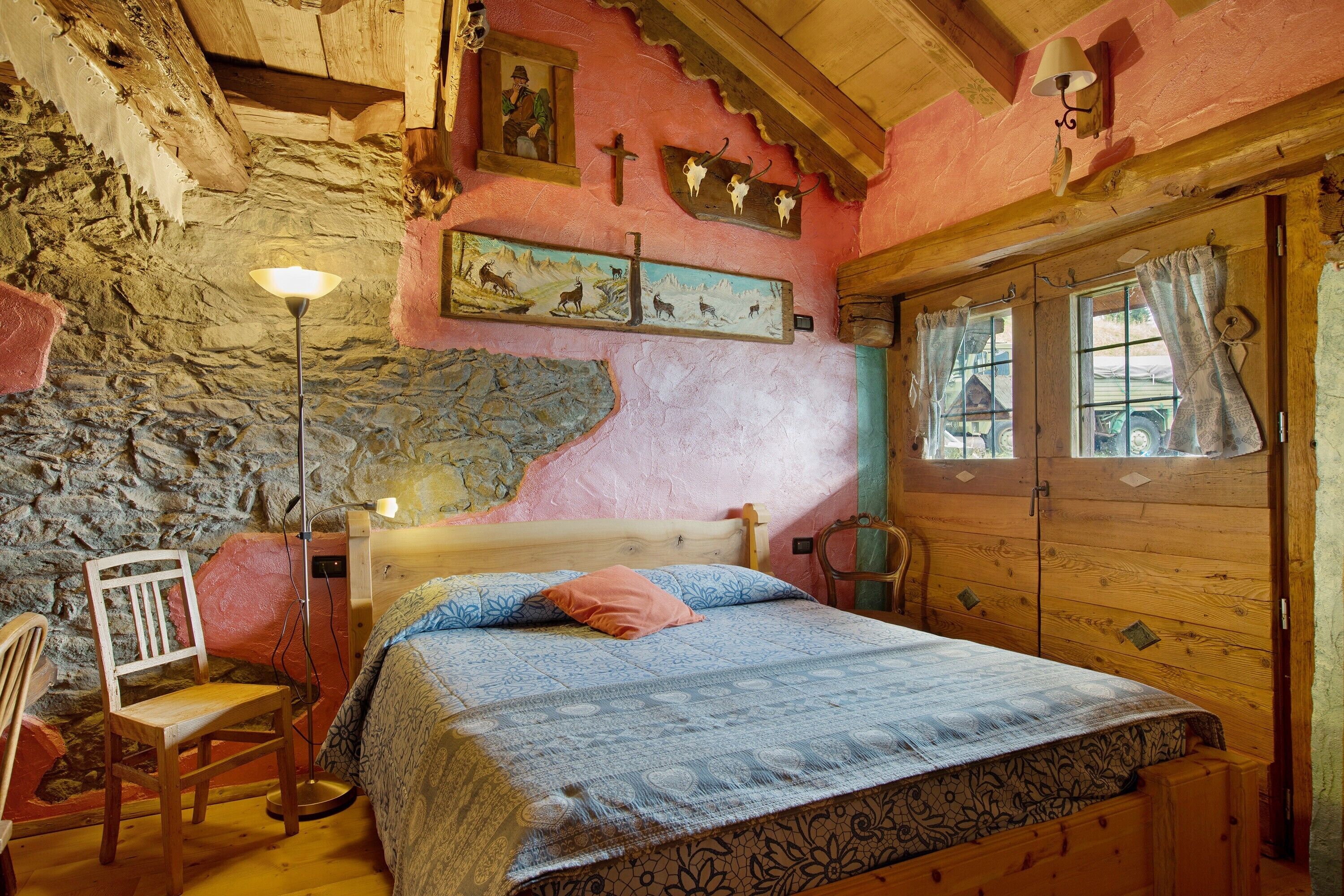 Ein rustikales Schlafzimmer mit Steinwand, Holzbett und einem einzelnen Stuhl.