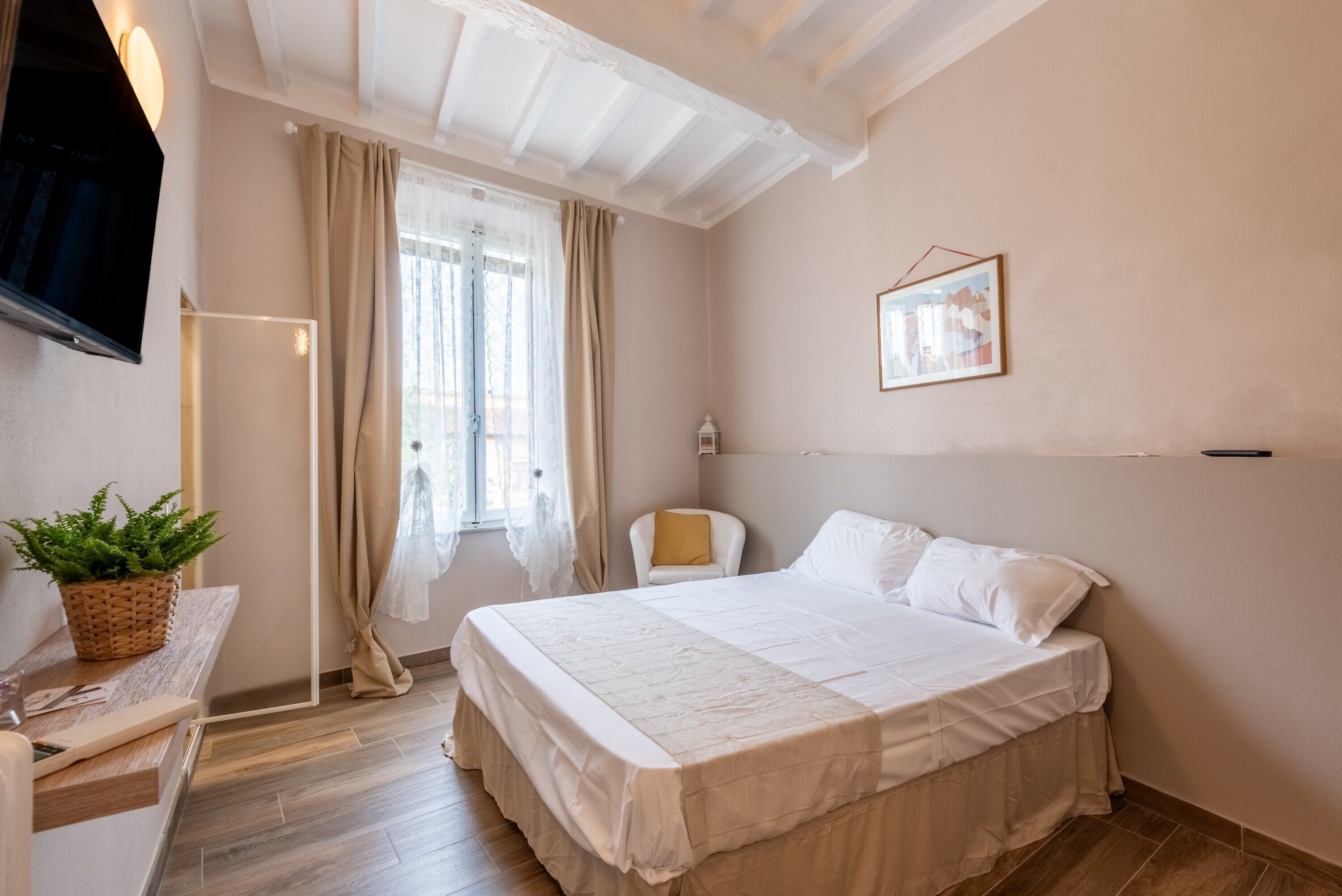 A bedroom with a bed, a chair, a TV, a window with curtains, and a wall-mounted picture.