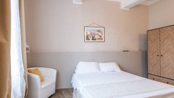 A bedroom with a bed, a chair, a wardrobe, and a framed picture on the wall.