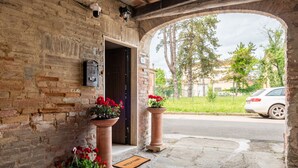 Entrada de un edificio de ladrillo con felpudo, macetas de flores rojas y buzón.