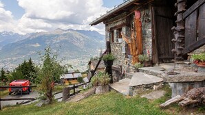 A rustic mountain cabin with stone walls, a wooden staircase, and a view of distant mountains. - Capriolo Room – Intimacy and Tranquility with Mountain Views (Charvensod)