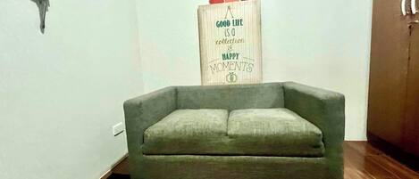 A living room with a grey sofa, a red and white patterned rug, and a wooden sign with a quote.