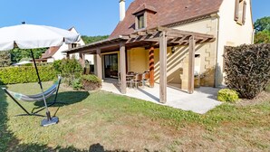 Ein Haus mit überdachter Terrasse, einer Hängematte und einem Tisch mit Stühlen.