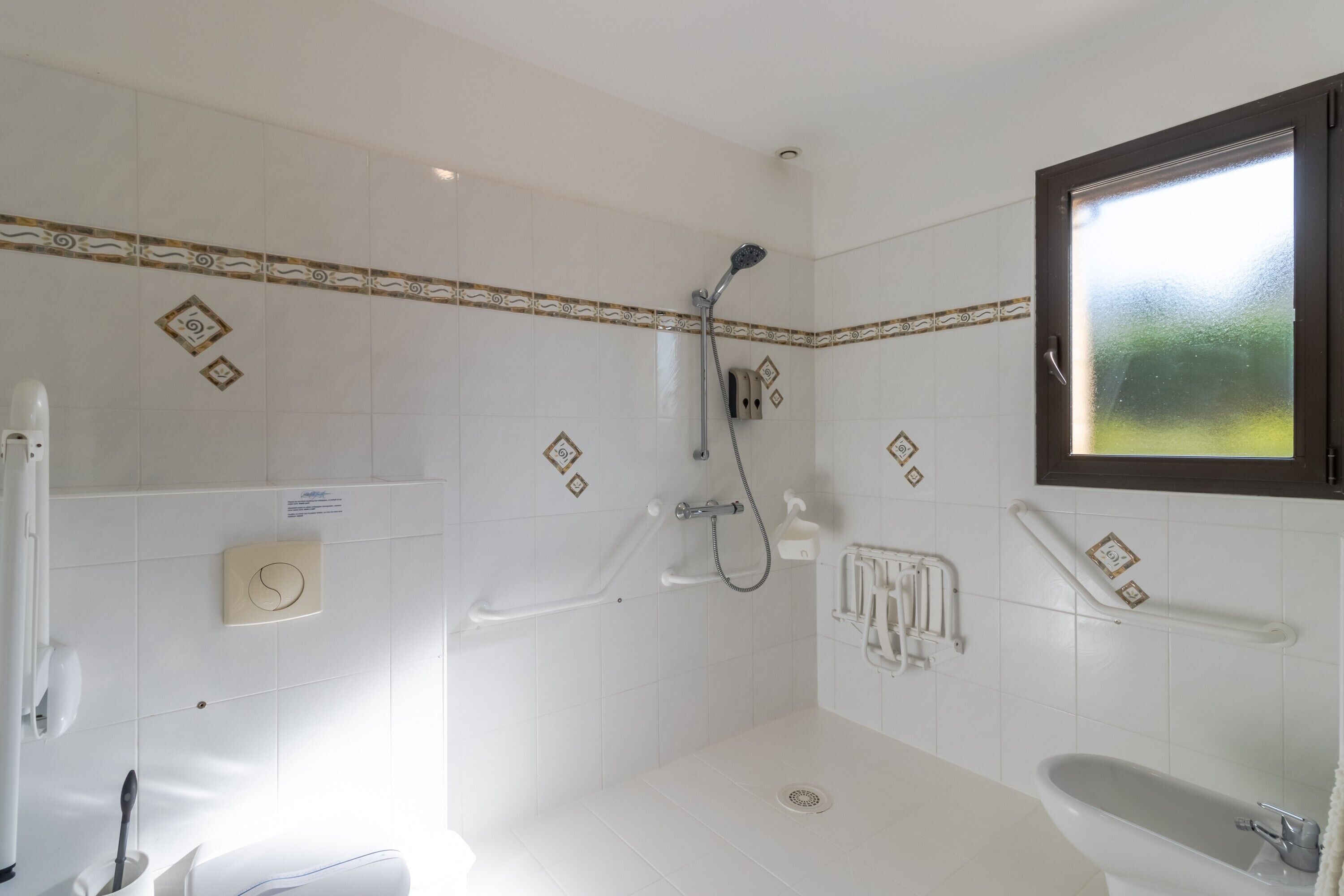 Een badkamer met witte tegels, een douche, toilet en wastafel.