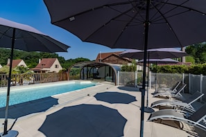 A swimming pool with lounge chairs and umbrellas, surrounded by a fence and houses in the background.