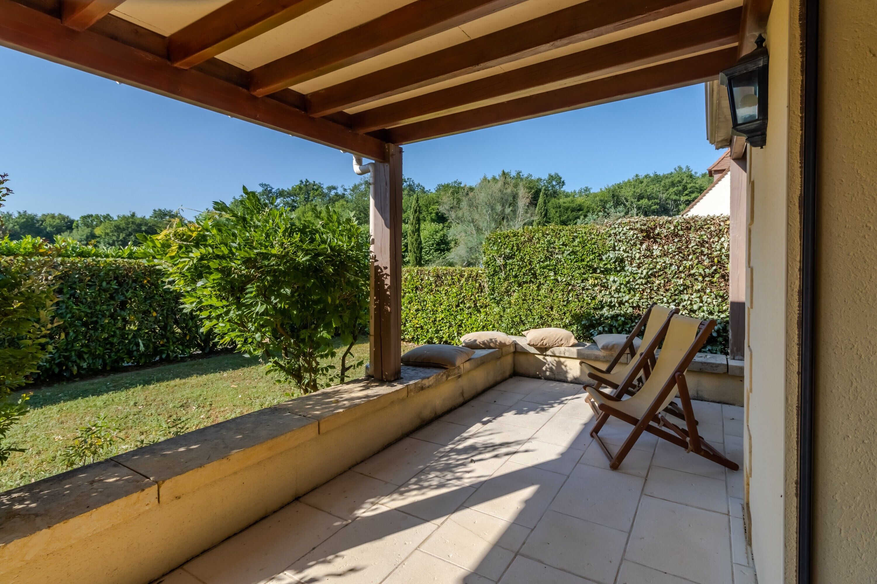 A covered patio with a view of a garden and a seating area with chairs.