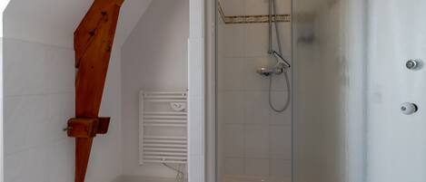 A shower with a glass door, a wooden beam, and a white tiled wall.