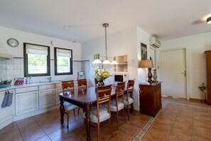A kitchen with a dining table, chairs, a clock, and a microwave.