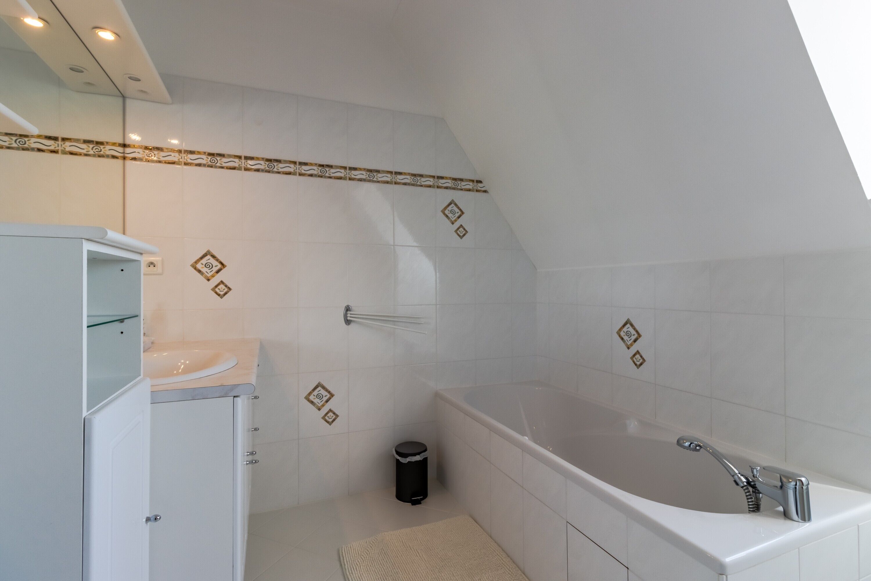 Een moderne badkamer met een bad, een wastafel met spiegel en een prullenbak.