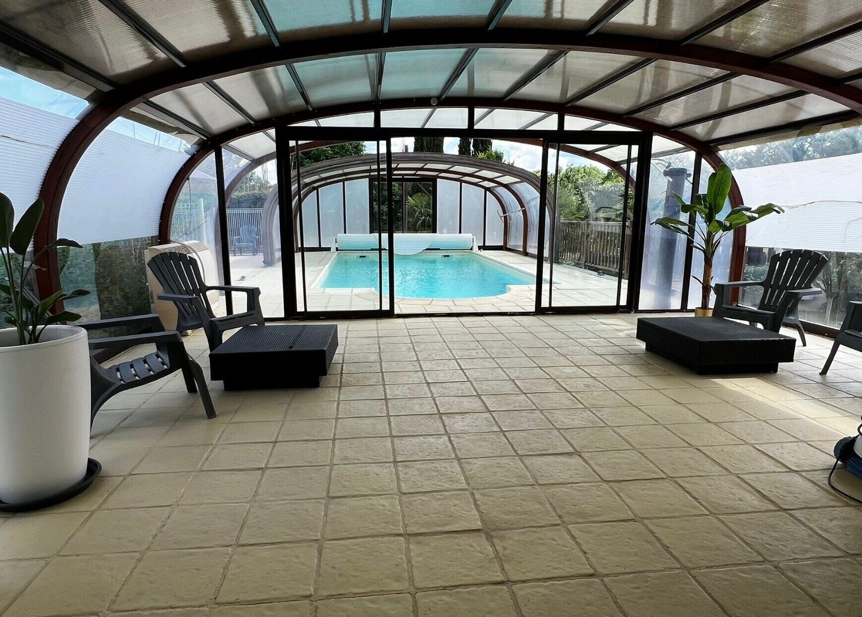 A covered outdoor area with a pool, lounge chairs, and potted plants.