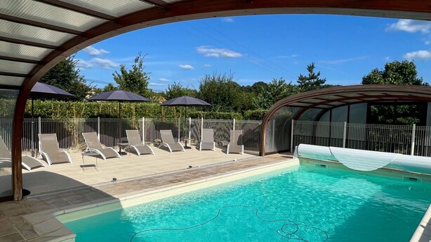 Une piscine entourée d’une clôture et d’arbres, avec des chaises longues et des parasols.