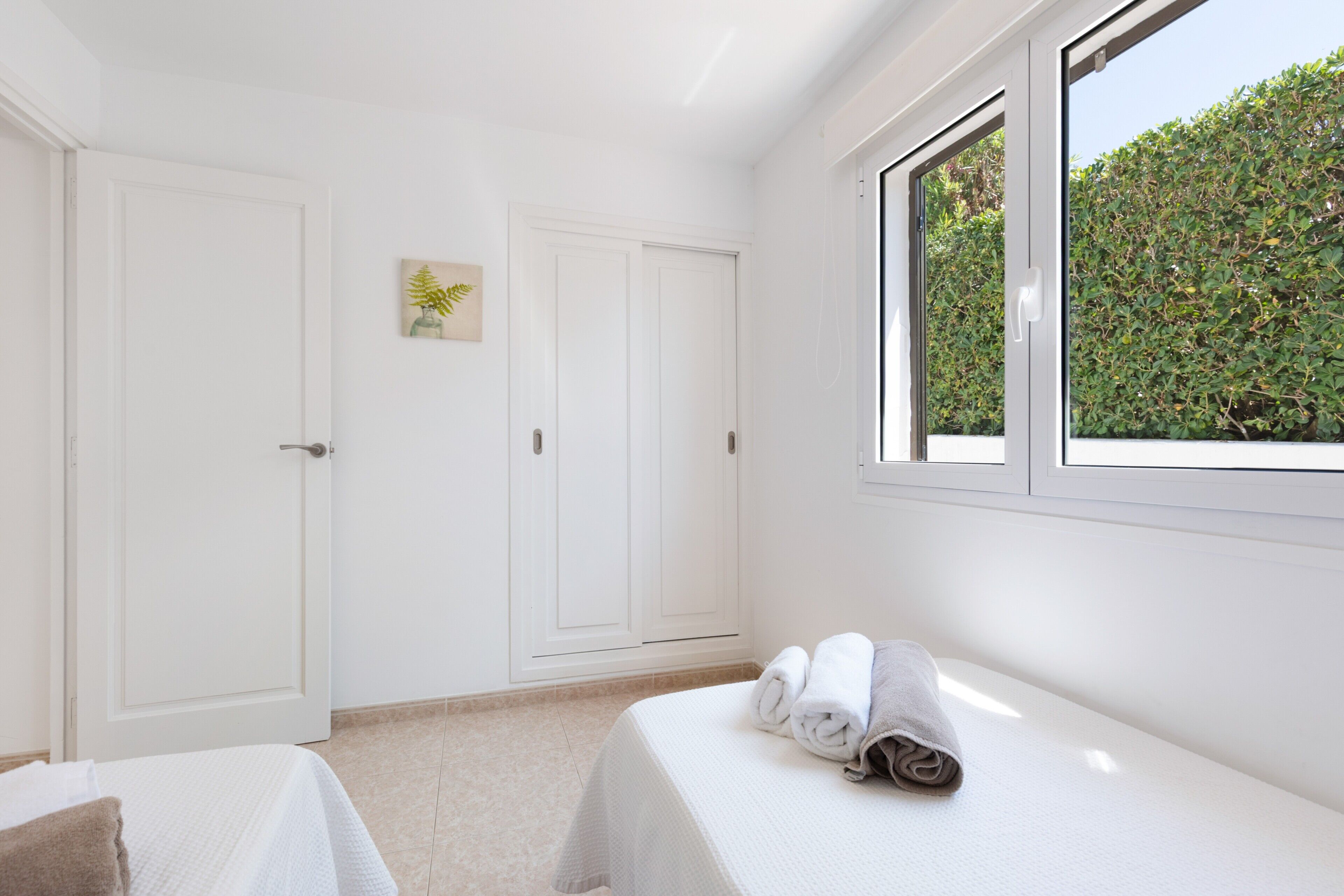 Un dormitorio con dos camas, una ventana que da a zonas verdes, paredes blancas y una puerta.