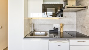 Una cocina moderna con un lavamanos de acero inoxidable, una placa de cocina por inducción negra y armarios blancos.