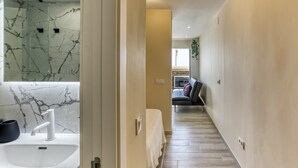 Un pasillo con pared de mármol, un lavamanos blanco y una cama con cubrecama blanco.