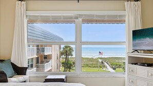 Un dormitorio con un amplio ventanal que ofrece vistas a la playa y un edificio al otro lado del agua.