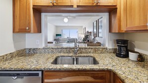 Una cocina con encimeras de granito, pileta de acero inoxidable, armarios de madera y cafetera.