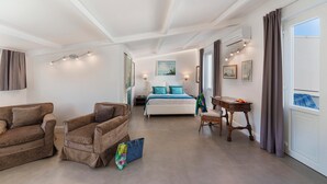 A spacious room with a bed, two armchairs, a small table, and a window with curtains.