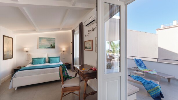 A bedroom with a bed, bedside table, chair, and a view of the balcony.